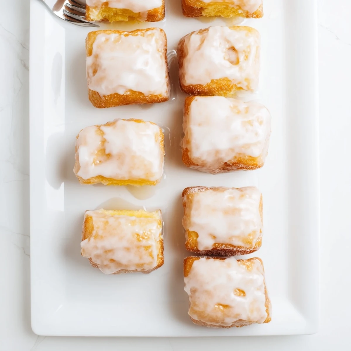 Golden glazed buttermilk beignet squares piled high on a serving platter with sweet vanilla icing dripping down the sides