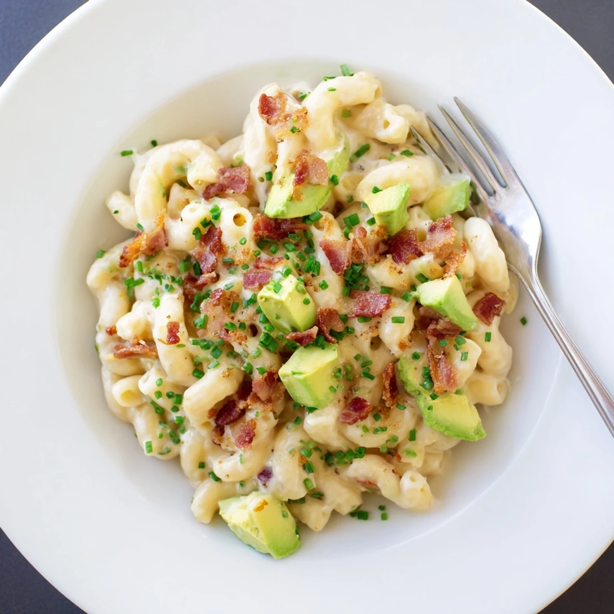 Creamy avocado and bacon mac and cheese topped with crispy bacon bits and fresh chives in a white bowl