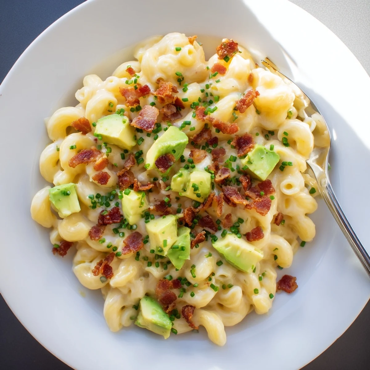Golden macaroni coated in rich cheddar sauce with diced avocado and smoky bacon scattered on top