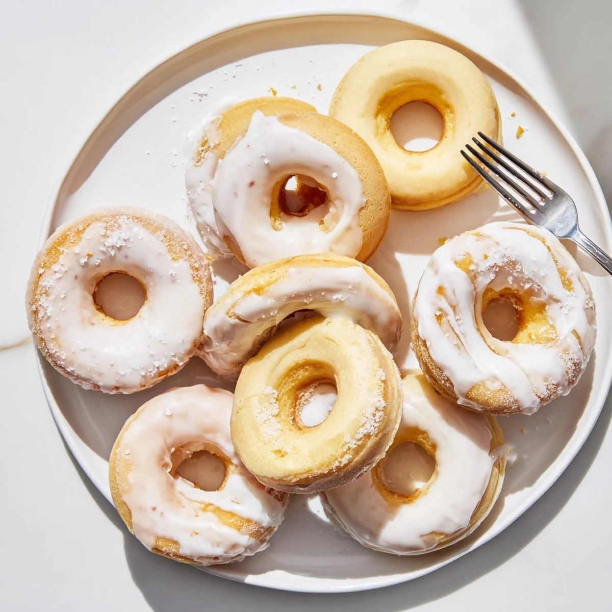 Freshly baked Greek yogurt cake donuts arranged on a white plate, topped with creamy white glaze