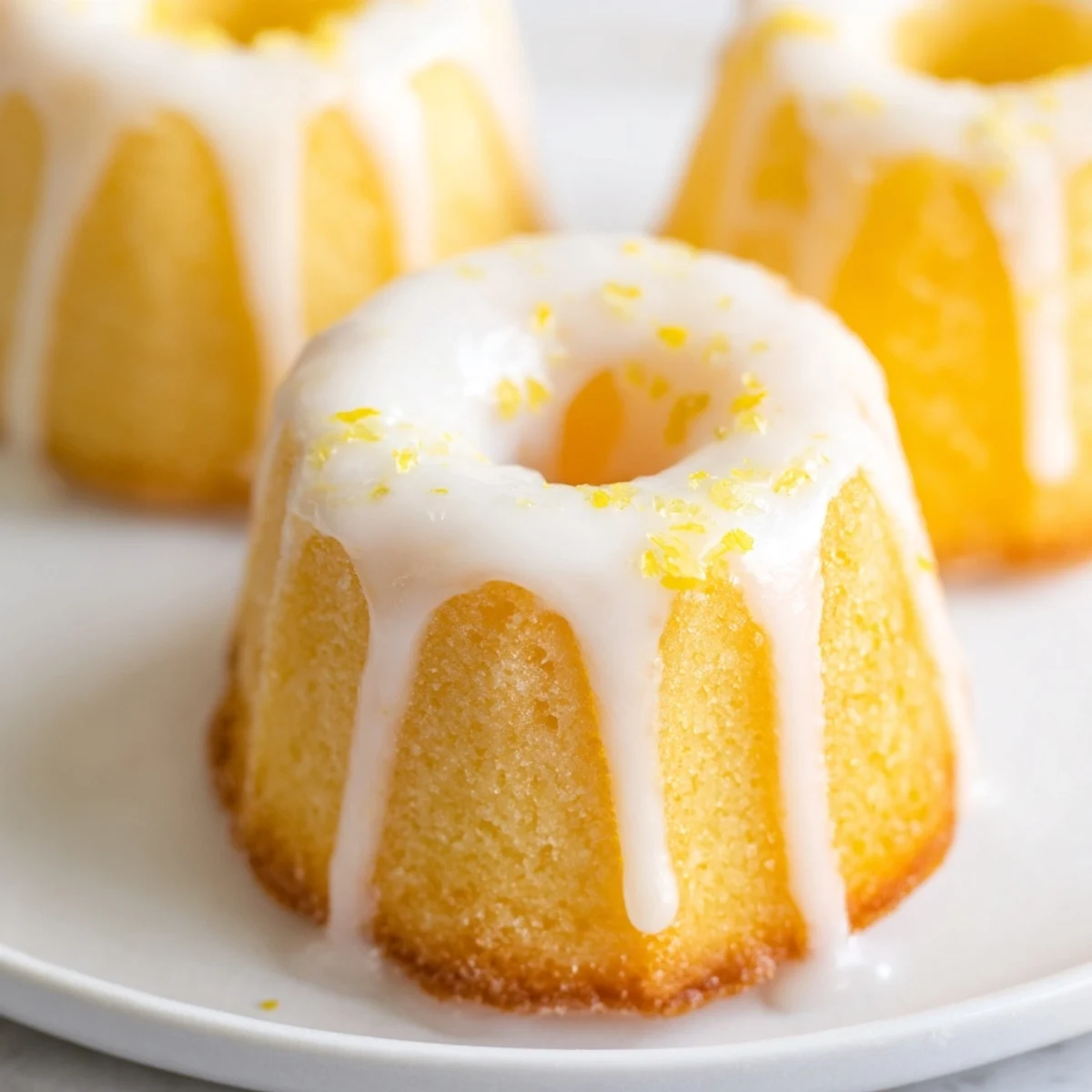 Golden mini lemon cakes drizzled with tangy glaze on a white serving plate