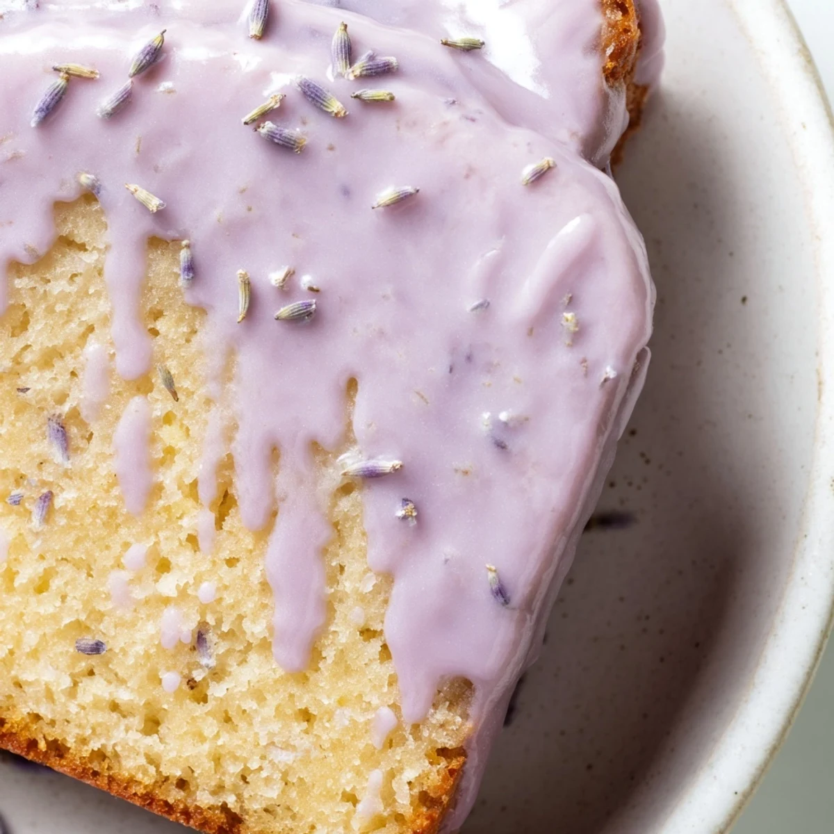 Smooth lavender glaze cascading over a vanilla pound cake slice on white ceramic plate