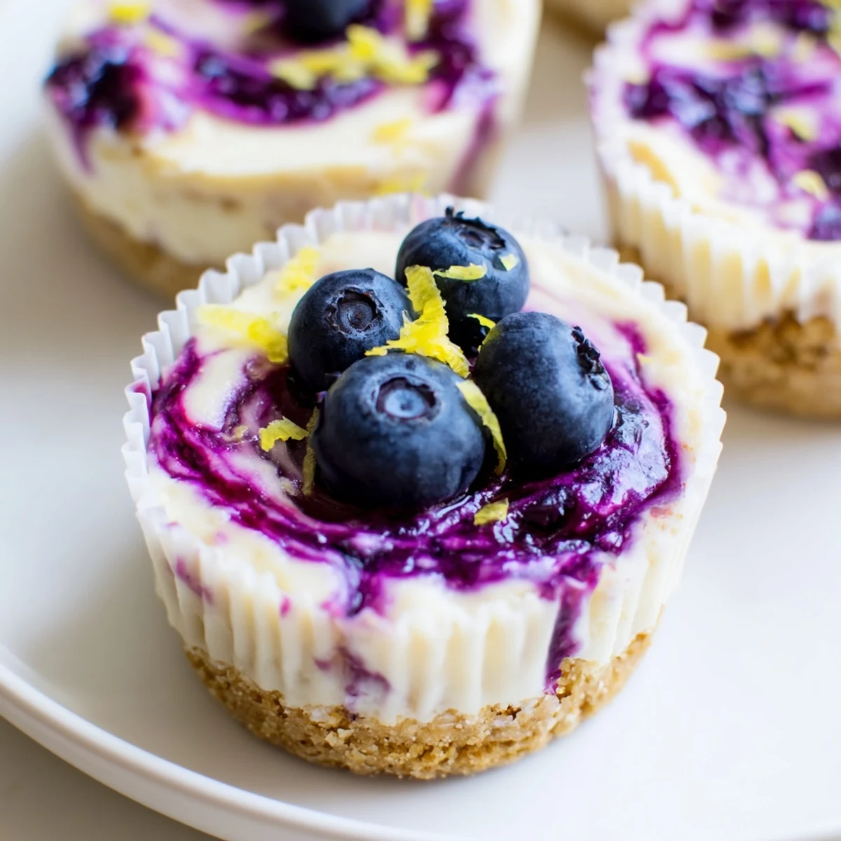 Creamy mini lemon blueberry cheesecakes with swirled berry topping on a graham crust