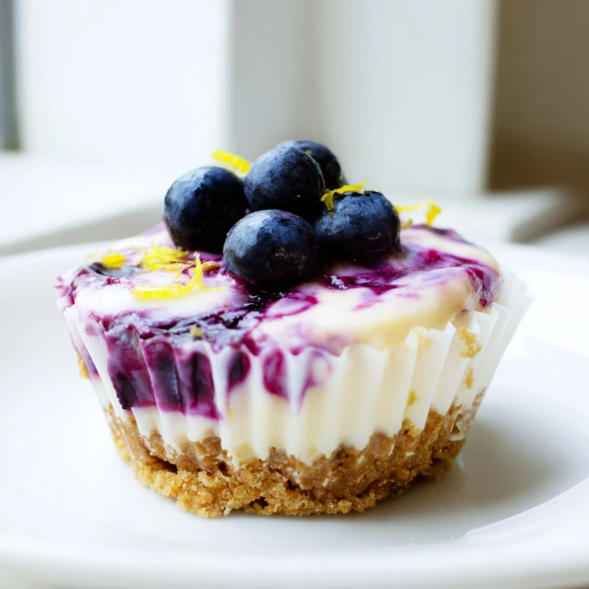 Individual mini lemon blueberry cheesecakes garnished with fresh berries and bright lemon zest
