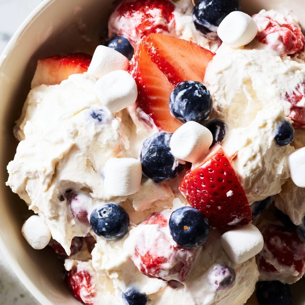 Vibrant Red White Blue Cheesecake Salad topped with juicy berries and pillowy mini marshmallows served chilled