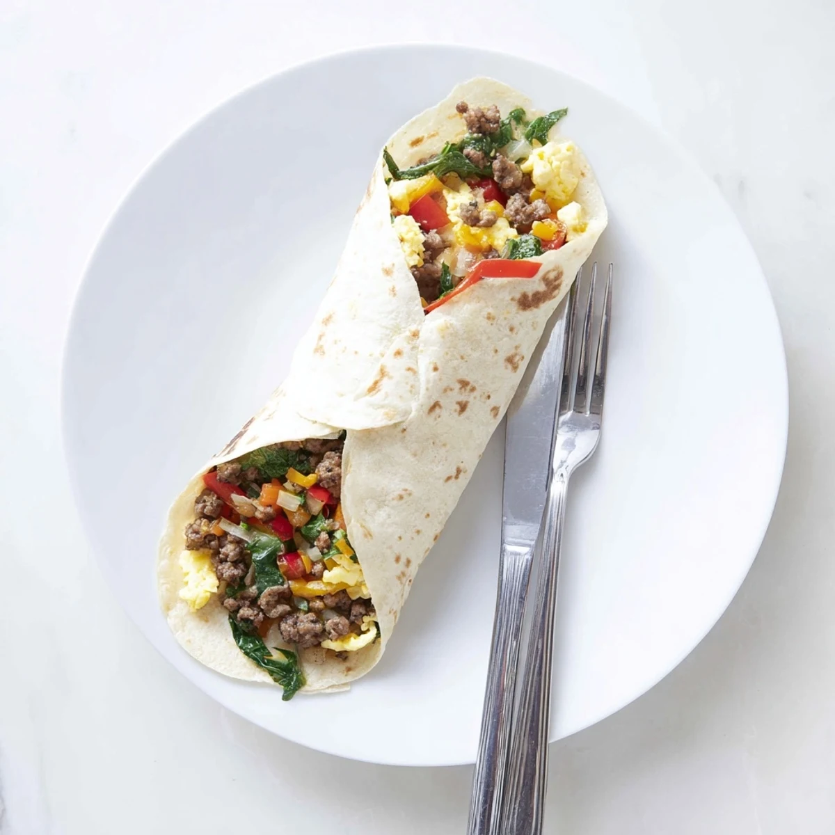 Rolled freezer breakfast burritos packed with savory sausage and fluffy eggs on a plate