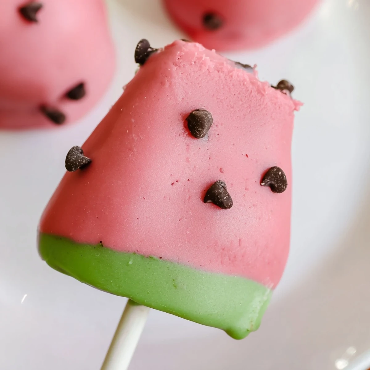 Pink watermelon cake pops on sticks with chocolate chip seeds and green rind