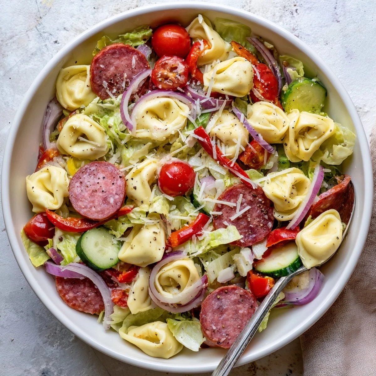 Hearty pasta salad featuring cheese tortellini, cherry tomatoes, roasted red peppers, provolone cubes, and tangy pepperoncini in a white serving bowl