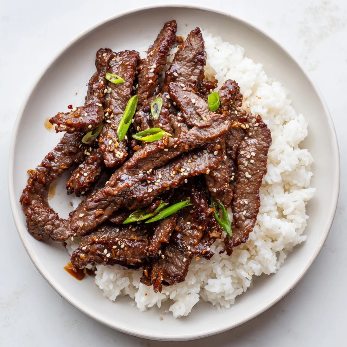 Korean Beef sizzling in a hot skillet, glossy sauce over rice