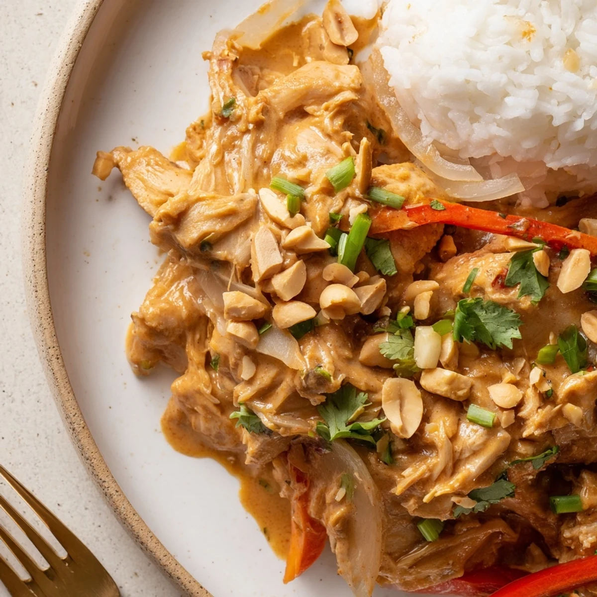 Crockpot Thai Peanut Chicken simmering in creamy sauce over jasmine rice, garnished