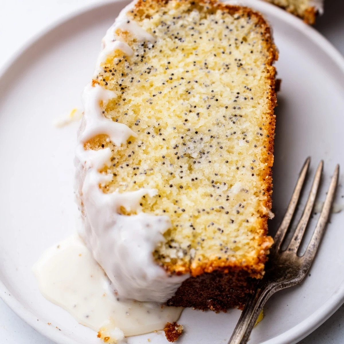 Moist lemon poppy seed cake slice showing tender crumb and scattered poppy seeds on white plate