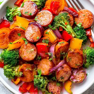 Smoky sliced kielbasa coated in sticky honey garlic glaze alongside caramelized roasted vegetables