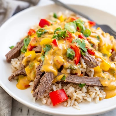 Golden seared steak strips nestled over fluffy steak queso rice with melted cheddar